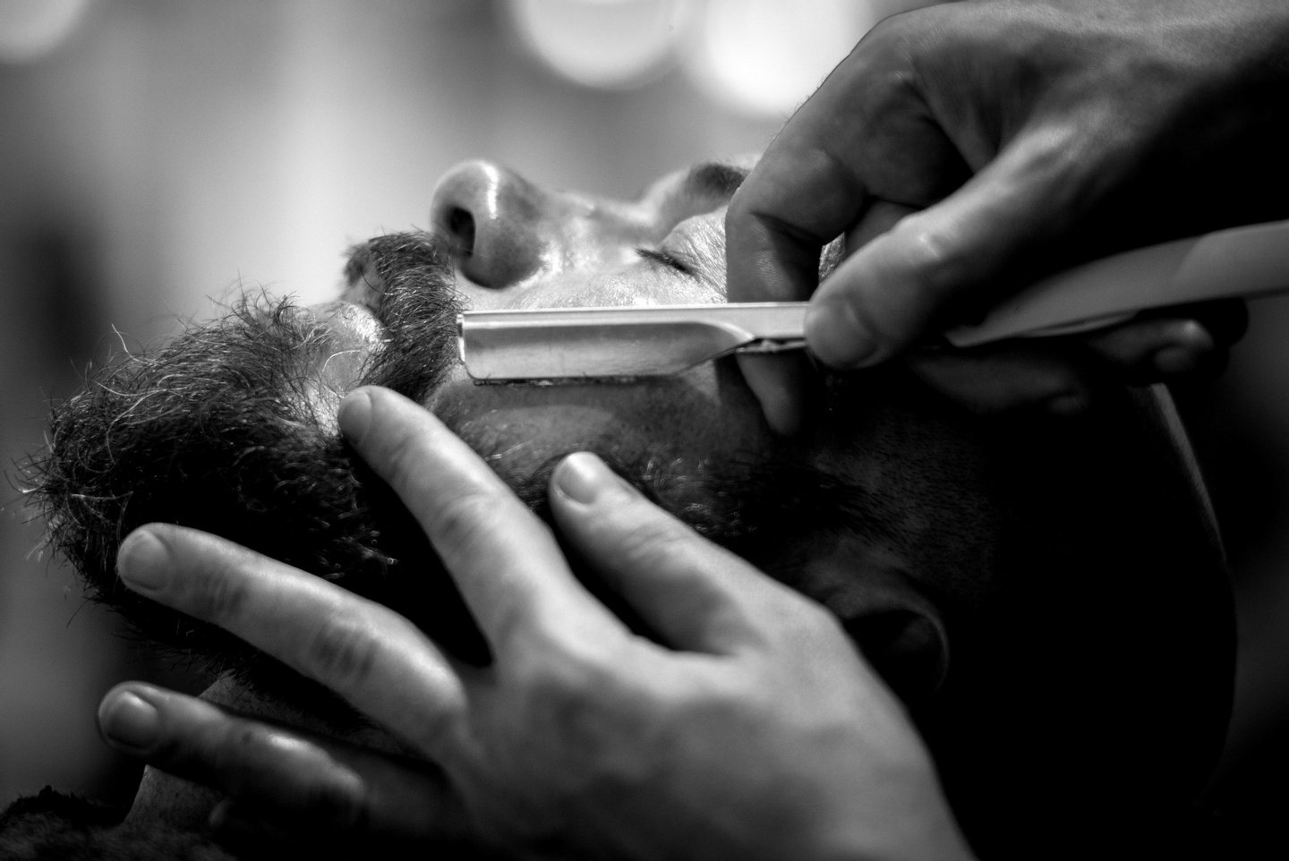 MANCHESTER, ENGLAND - APRIL 29: (EDITORS NOTE: This image has been converted to black and white. Colour version available upon request.) Barber Ricky Trim wet shaves a customer in Manchester's Barber Barber, a 'gentleman's saloon' style male barber shop, on April 29, 2015 in Manchester, England. According to owner Johnny the Baba, Barber Barber is the UK's finest barber shop. The shop for 'gentleman and scoundrels' takes a traditional approach to male grooming, and offers services such as wet shaving, beard scultping and highly skilled hair styling. The shop also offers complimentary drinks and cigars to it's customers and operates a 'gentlemen only' door policy. (Photo by Christopher Furlong/Getty Images)