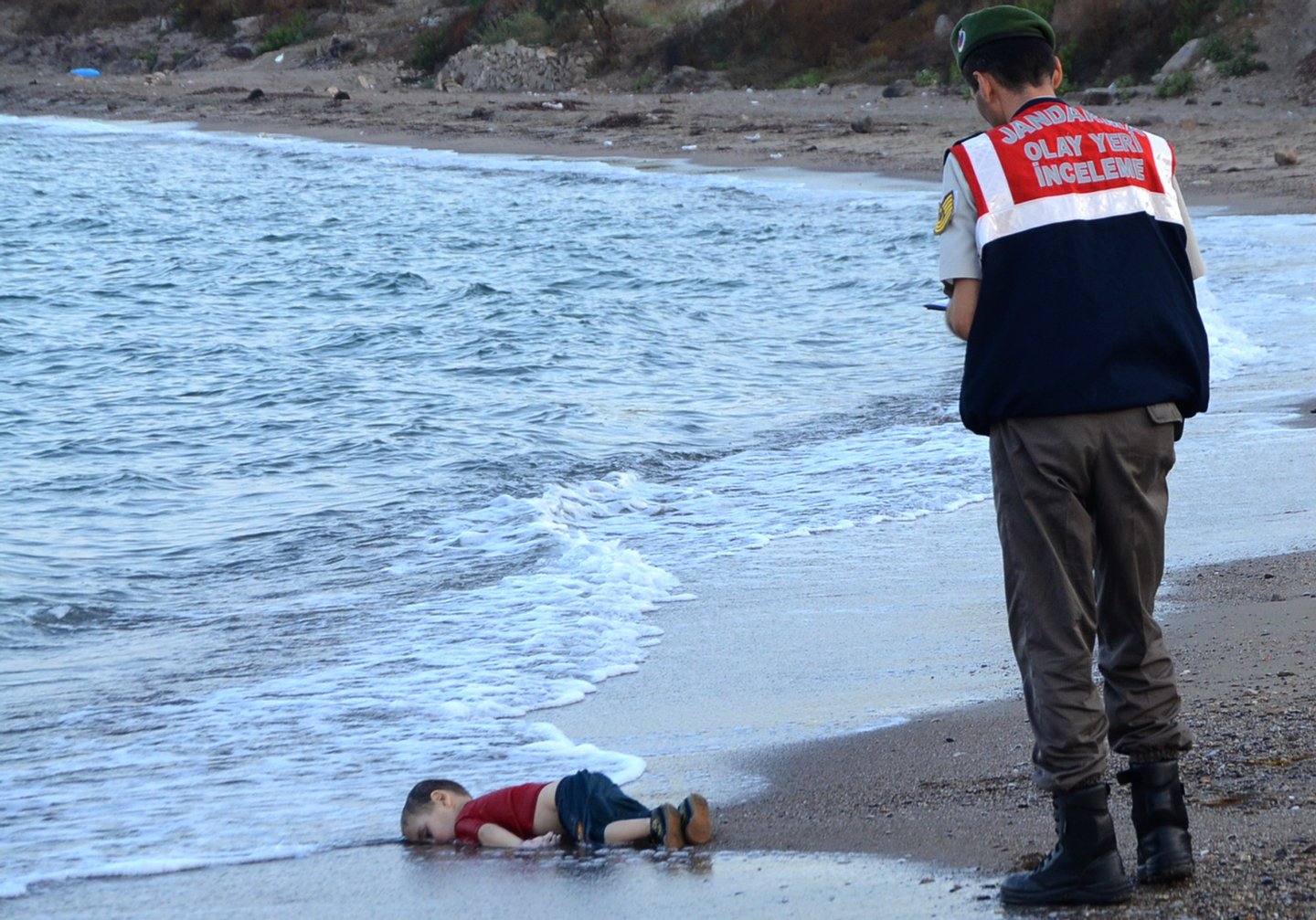 GRAPHIC CONTENT A Turkish police officer stands next to a migrant child's dead body (Aylan Shenu) off the shores in Bodrum, southern Turkey, on September 2, 2015 after a boat carrying refugees sank while reaching the Greek island of Kos. Thousands of refugees and migrants arrived in Athens on September 2, as Greek ministers held talks on the crisis, with Europe struggling to cope with the huge influx fleeing war and repression in the Middle East and Africa. / AFP / DOGAN NEWS AGENCY / Nilufer Demir (Photo credit should read NILUFER DEMIR/AFP/Getty Images)