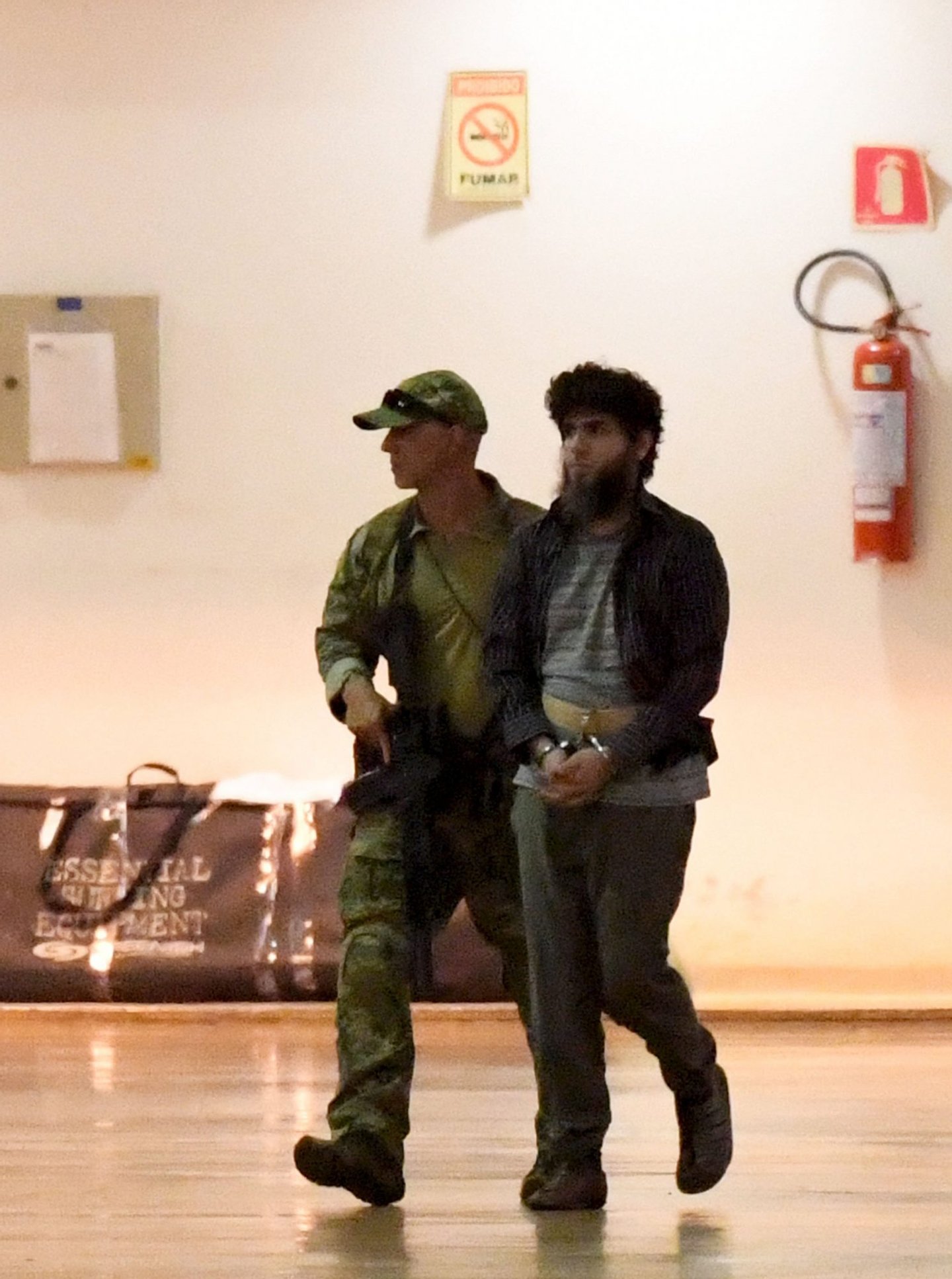 An alleged terrorist walks escorted by police at the Brazilian Federal Police hangar at the airport in Brasilia on July 21, 2016. Brazilian police have arrested 10 members of an "amateur" would-be terrorist group that expressed loyalty to the Islamic State organization and was targeting the upcoming Olympics, officials said. / AFP / EVARISTO SA (Photo credit should read EVARISTO SA/AFP/Getty Images)